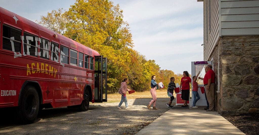 Students head into a building walking off a red school bus with "LifeWise" on the side.