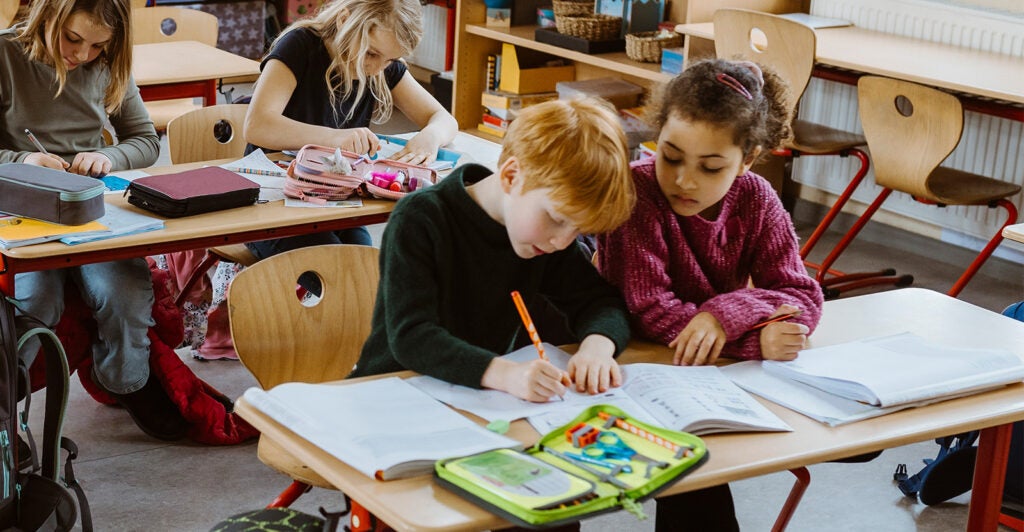 Elementary students sit at tables in a classroom working on a project together.