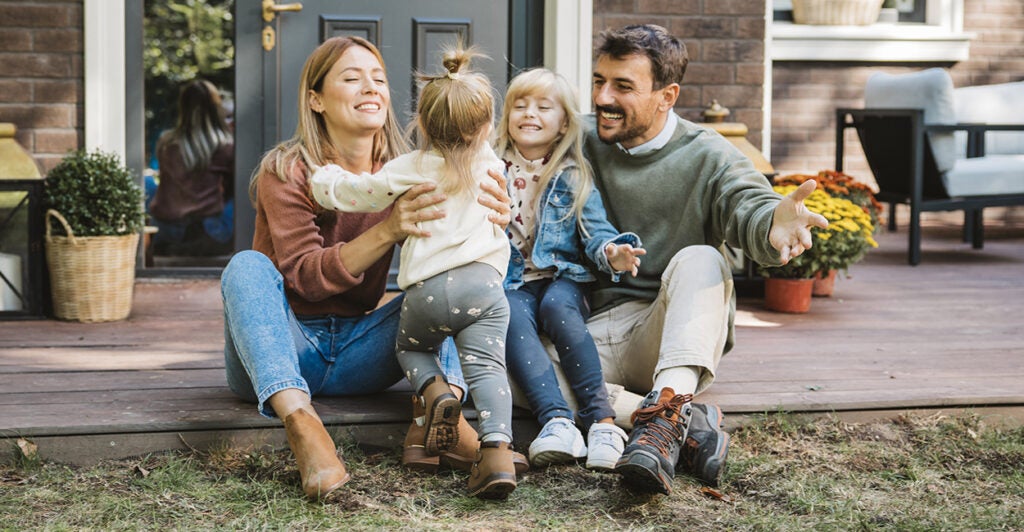 Young couple and their two young kids laughing and smiling, sitting on their porch.