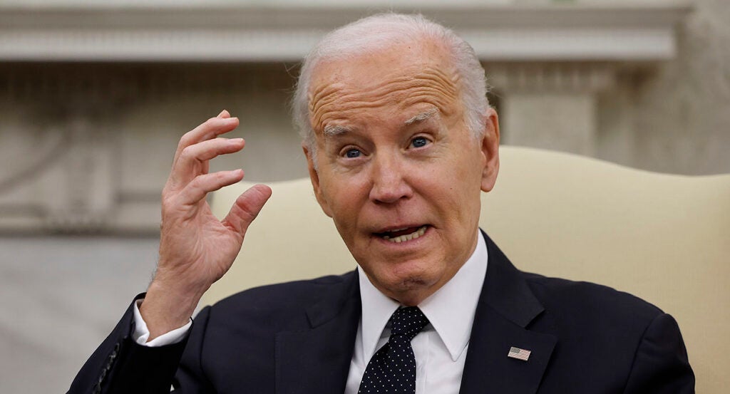 President Joe Biden in a suit with an American flag pin holds his hand near his head