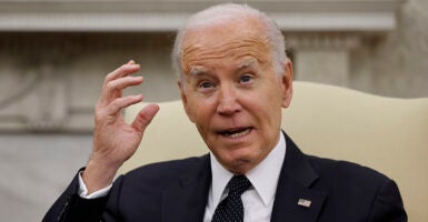 President Joe Biden in a suit with an American flag pin holds his hand near his head