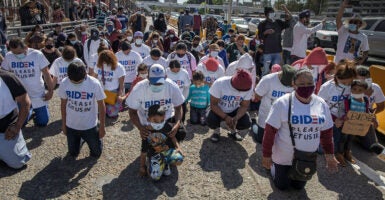 Migrants kneel wearing t-shirts reading "Biden please let us in" near the U.S.-Mexico border.