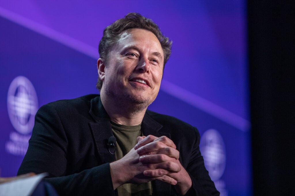 Billionaire Elon Musk smiling in front of a blue background