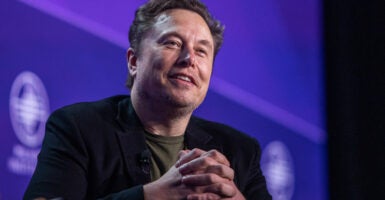 Billionaire Elon Musk smiling in front of a blue background