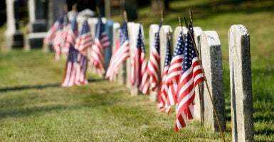 American flags seen flying in front of a row of tombstones.