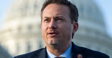 Rep. Michael Cloud speaks outside in a suit with the Capitol behind him.