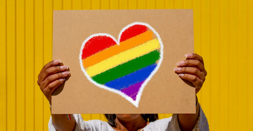 A woman holds a rainbow heart sign.