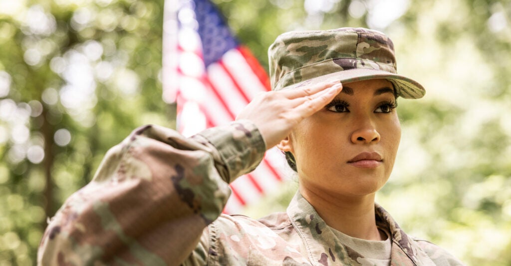 A female U.S. soldier saluting in front of an American flag.