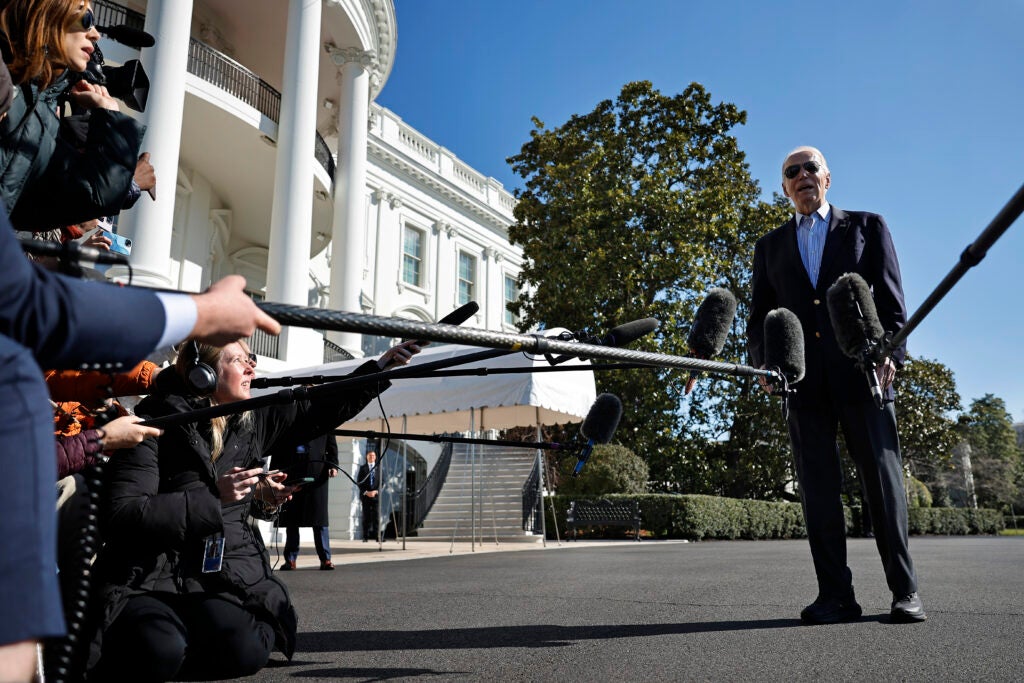 Joe Biden talks to reporters extending microphones to him in front of the White House.