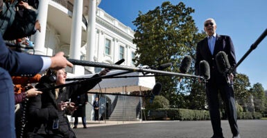 Joe Biden talks to reporters extending microphones to him in front of the White House.