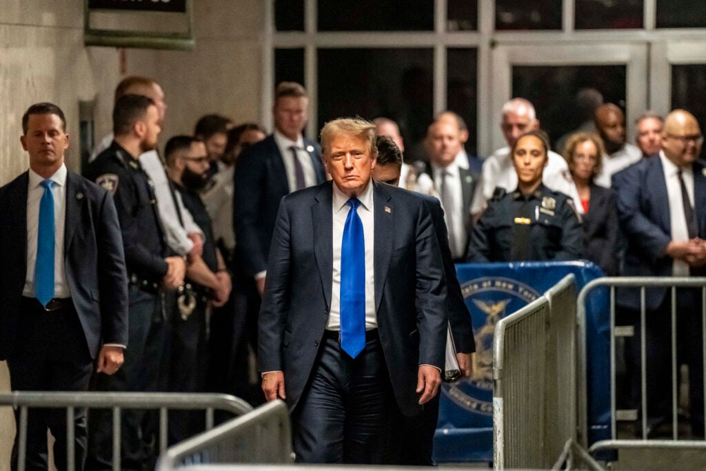 Donald Trump walks toward the camera wearing a blue tie and suit.