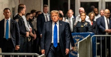 Donald Trump walks toward the camera wearing a blue tie and suit.