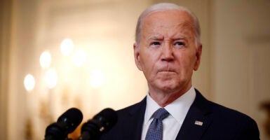 Joe Biden stands in front of a microphone wearing a suit and blue tie.