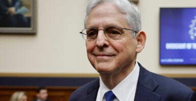 Attorney General Merrick Garland smiles as he enters a room, wearing a blue suit and tie.