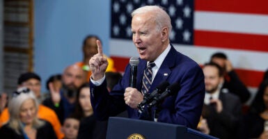 President Joe Biden in a blue suit raises a finger while speaking in a microphone