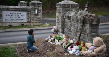 A woman kneeling and praying in front of a memorial.