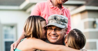 Two children hug their father who is wearing an army uniform while his wife stands over them.