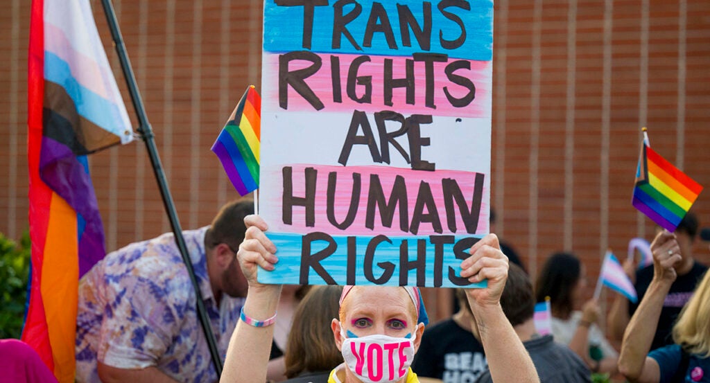 Woman holds sign reading "Trans Rights Are Human Rights" while wearing a face mask with the text "Vote."