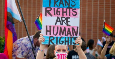 Woman holds sign reading "Trans Rights Are Human Rights" while wearing a face mask with the text "Vote."