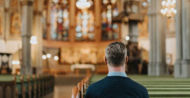 A man sits in a pew in a Catholic cathedral.