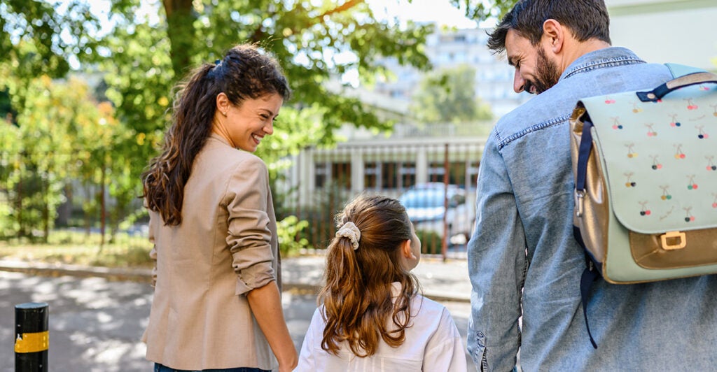 A mom, dad, and daughter hold hands and walk.