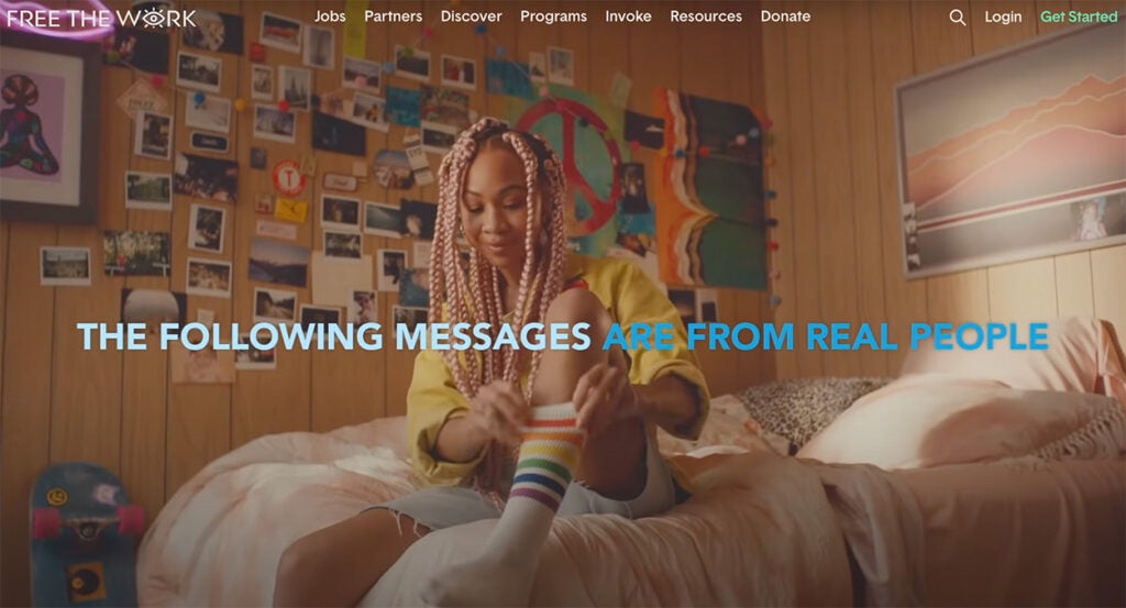 A girl puts on a rainbow-patterned sock while sitting on her bed.