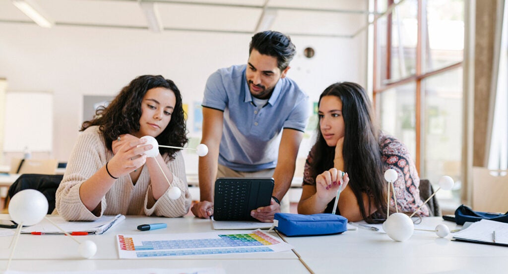 Three high school science students look at models in class.