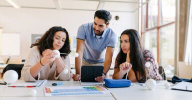 Three high school science students look at models in class.