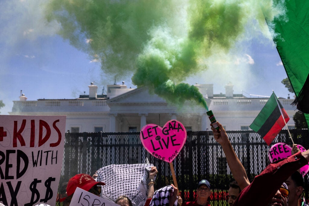 Protesters spraying green smoke and holding signs in front of the White House lawn.