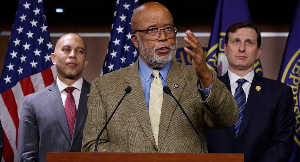 Bennie Thompson in a brown suit gestures in front of an American flag