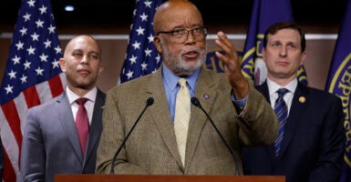 Bennie Thompson in a brown suit gestures in front of an American flag