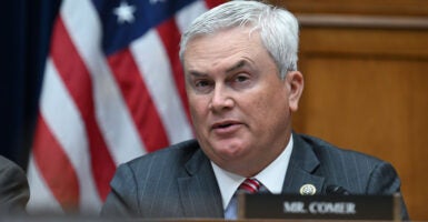 House Oversight Chairman James Comer in a suit sitting in a committee hearing in front of the American flag