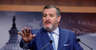 Ted Cruz speaks at a podium into a microphone with an outstretched hand.