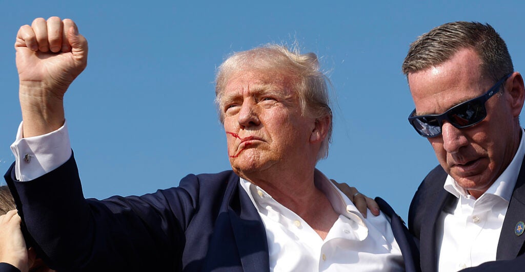 Republican presidential candidate former President Donald Trump pumps his fist as he is rushed offstage by U.S. Secret Service agents after being grazed by a bullet during a rally on July 13, 2024 in Butler, Pennsylvania. Butler County district attorney Richard Goldinger said the shooter is dead after grazing former U.S. President Donald Trump with a bullet, killing one audience member and injuring another in the shooting. (Photo by Anna Moneymaker/Getty Images)