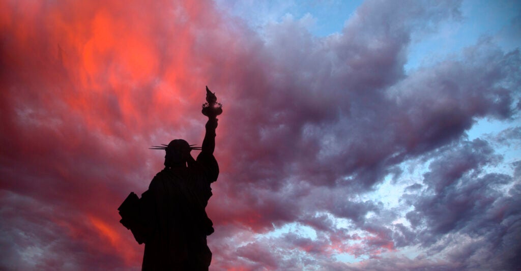 A silhouette of the Statue of Liberty with a sunset background.