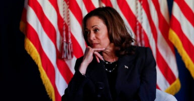 Vice President Kamala Harris looks left while wearing a blazer in front of an American flag.