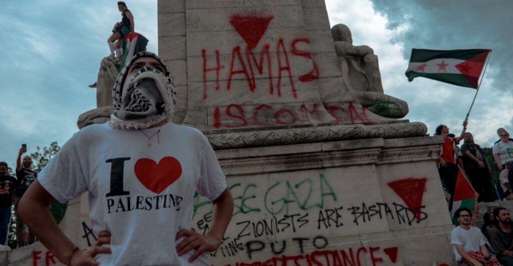 A protester wearing an "I love Palestine" T-shirt and standing in front of a monument.