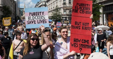 Protesters march with signs reading "Puberty Blockers Save Lives" and "Puberty Blockers for Cis Kids but Not Trans Kids"