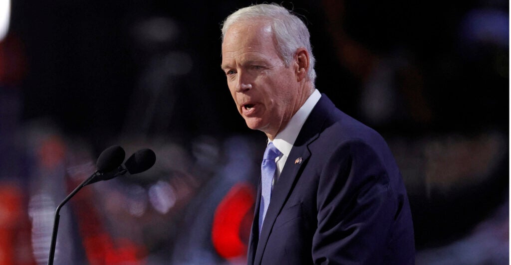 Senator Ron Johnson in a suit speaks to a large audience