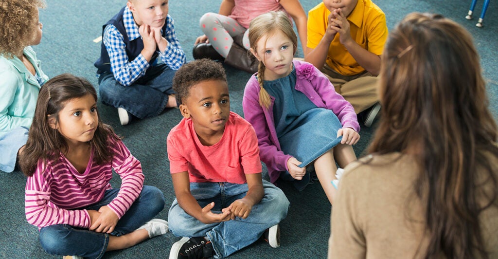 Kids sit in front of a teacher.