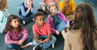 Kids sit in front of a teacher.