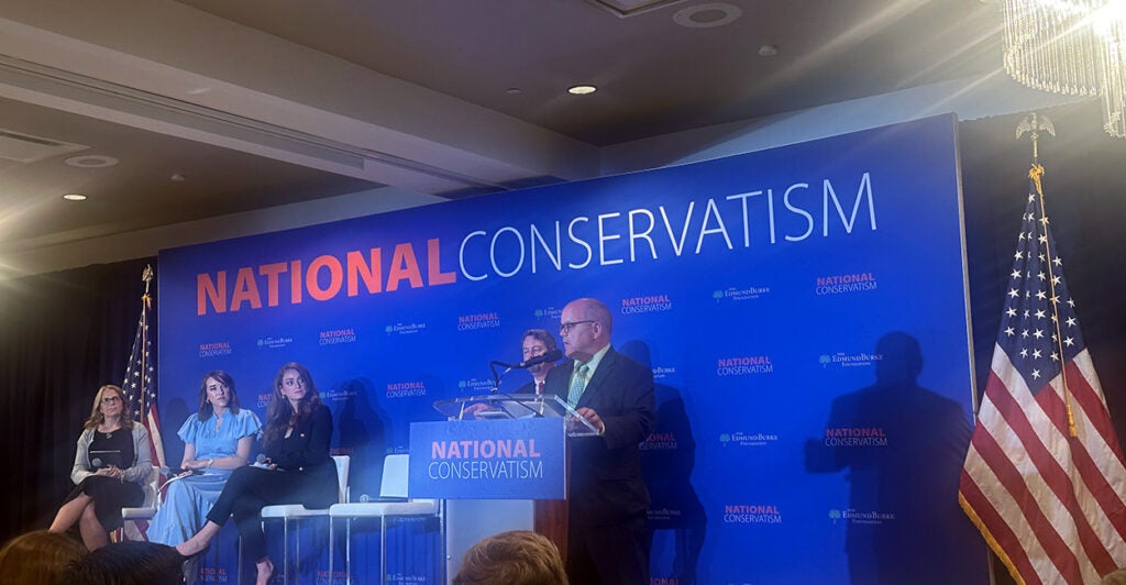 A man speaks in a microphone, while three women sit next to him on a panel,