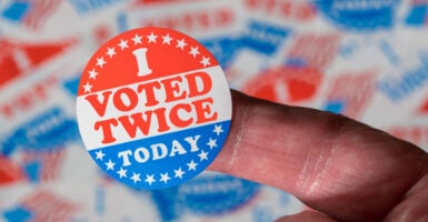 A finger holding an “I Voted Twice Today” sticker.