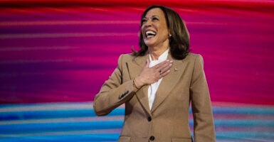 Kamala Harris on stage in a light brown suit smiling with her hand over her heart