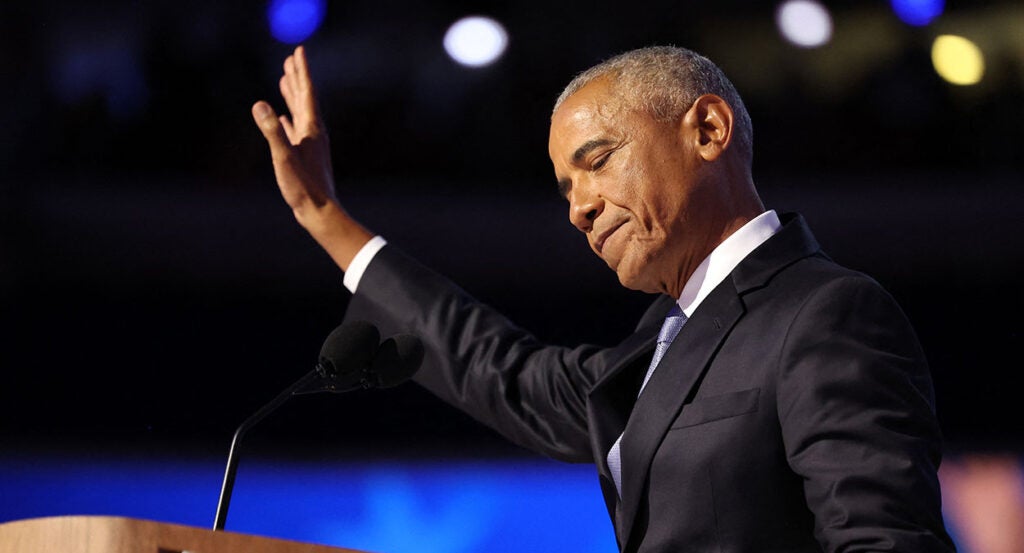 Barak Obama in a black suit raises his hand