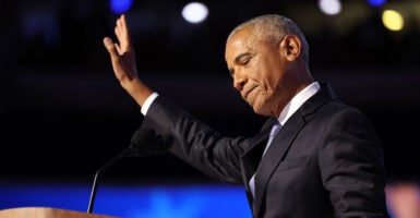 Barak Obama in a black suit raises his hand