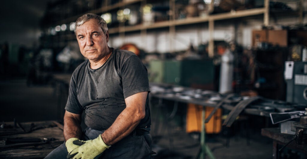 Mature man sits in factory workshop alone.