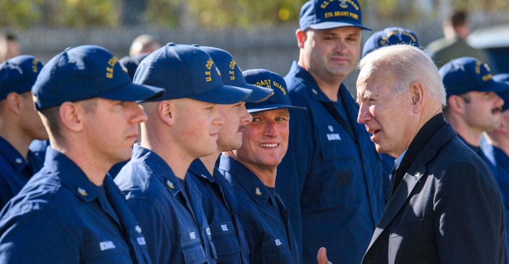 Coast Guard members in blue uniforms line up for inspection by President Joe Biden