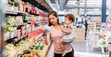 A young mother holds her daughter on her hip as she goes grocery shopping.