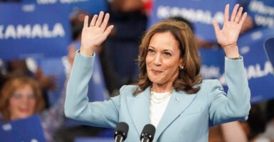 Kamala Harris wears a blue blazer and hold both hands up to a crowd.